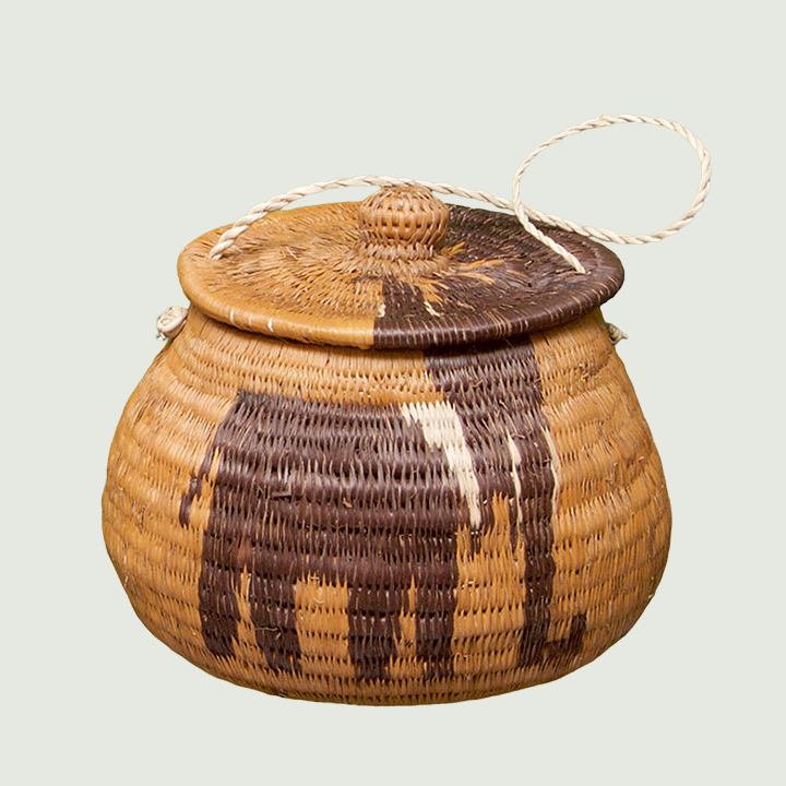 A handcrafted woven basket with a lid, decorated with dark patterns resembling an animal, and featuring a rope handle.