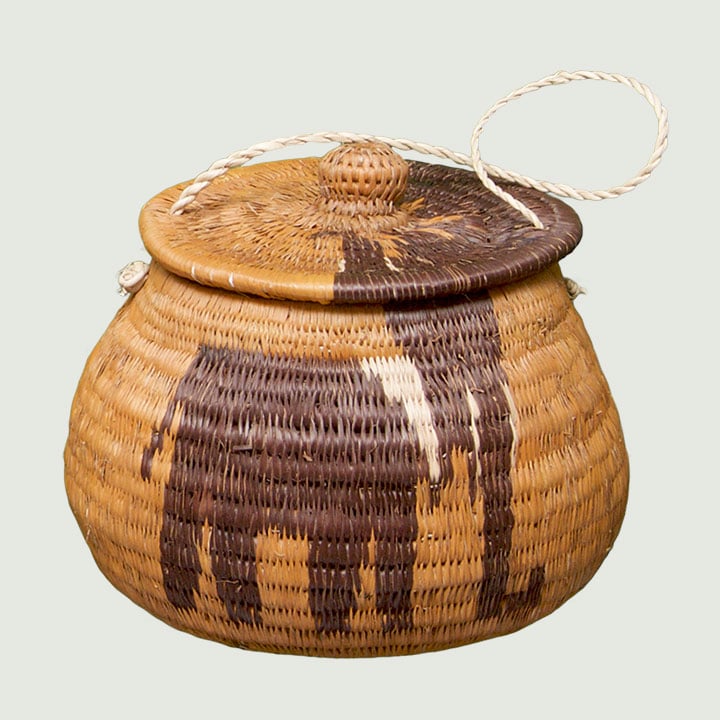 The image shows a woven basket with a lid, decorated with a design resembling an animal, and a braided handle attached to the lid.