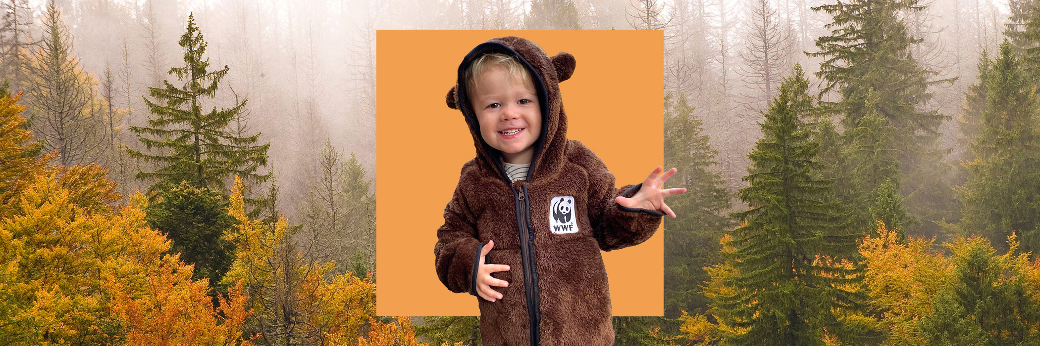 Little boy in brown bear fleece makes clawing action, in front of yellow square, in front of autumn trees