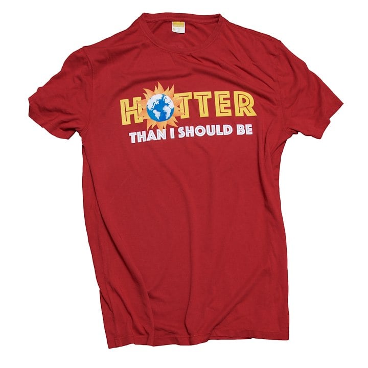A red shirt with bubbly font "Hotter than i should be" O in Hotter is an Earth enveloped by the sun