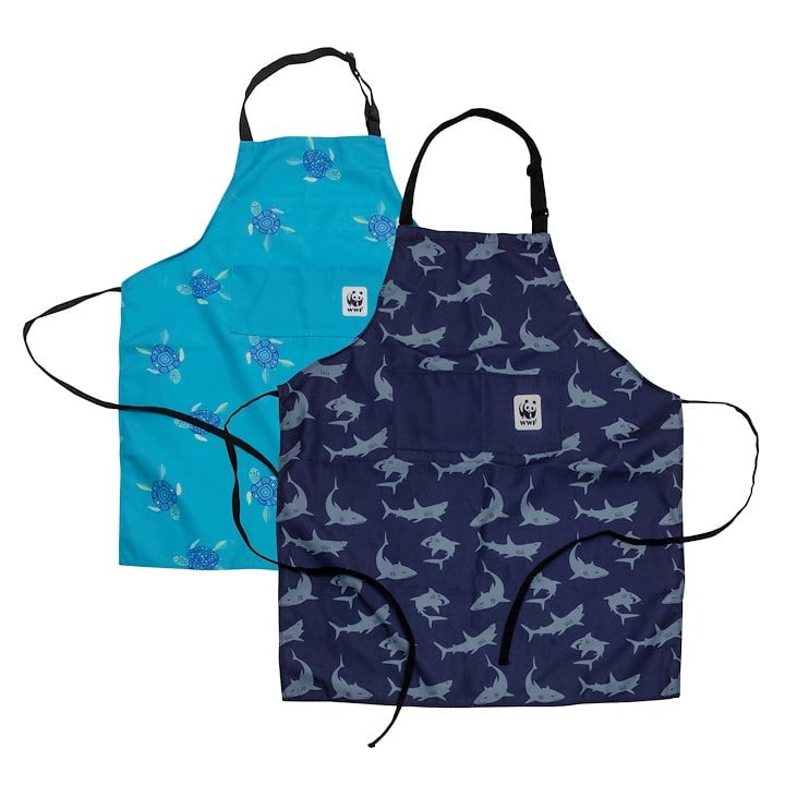 Two aprons, one blue with turtle patterns and the other dark blue with shark patterns, featuring black straps and a front pocket.